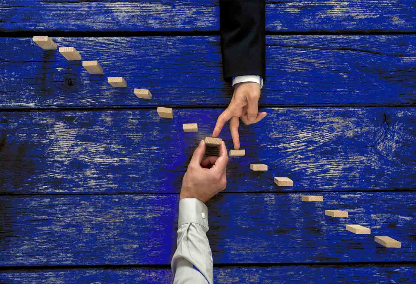 Businessman supporting wooden step in a staircase made of pegs as his partner walks his fingers up towards